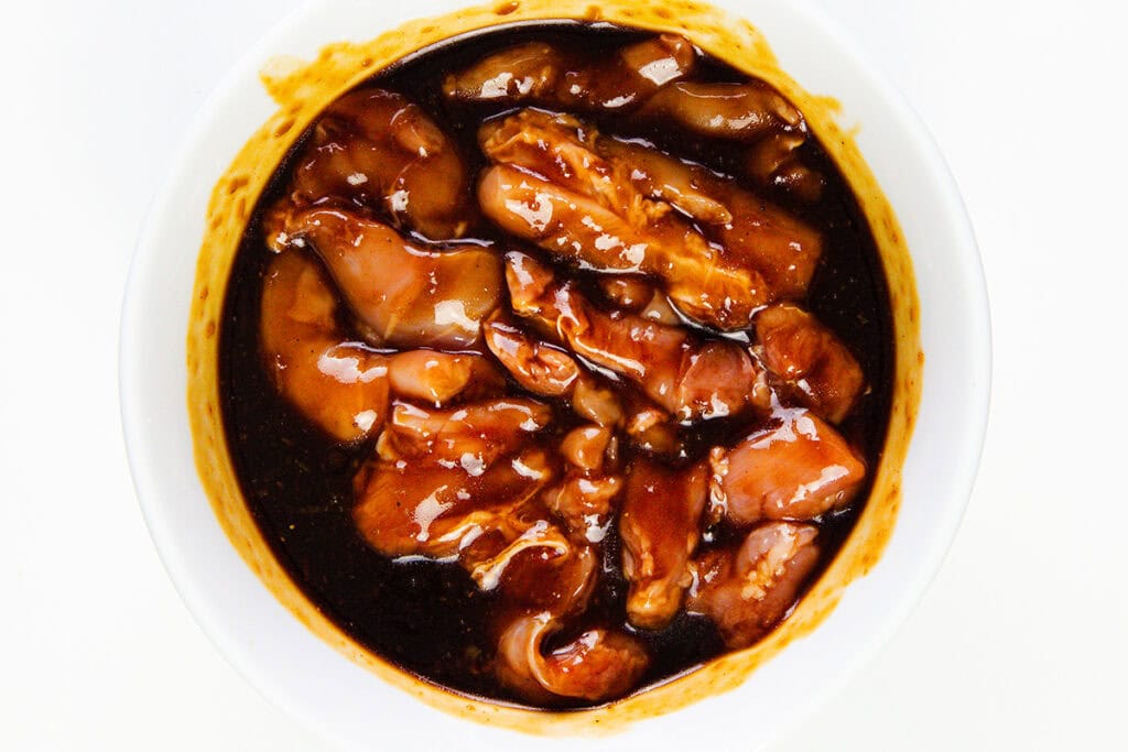 Sticky Asian BBQ Chicken Thighs marinated in a thick, dark brown sauce inside a white bowl, viewed from above.