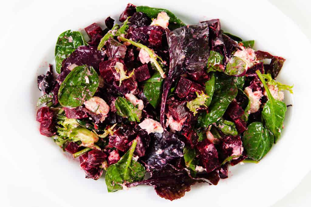 A plate of Beet Goat Cheese Salad with leafy greens, diced beets, crumbled cheese, and fresh herbs, all mixed together and served on a white dish.