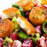 A close-up of a salad with crispy Fried Goat Cheese medallions, mixed greens, and cubed roasted beets, all garnished with chopped chives.