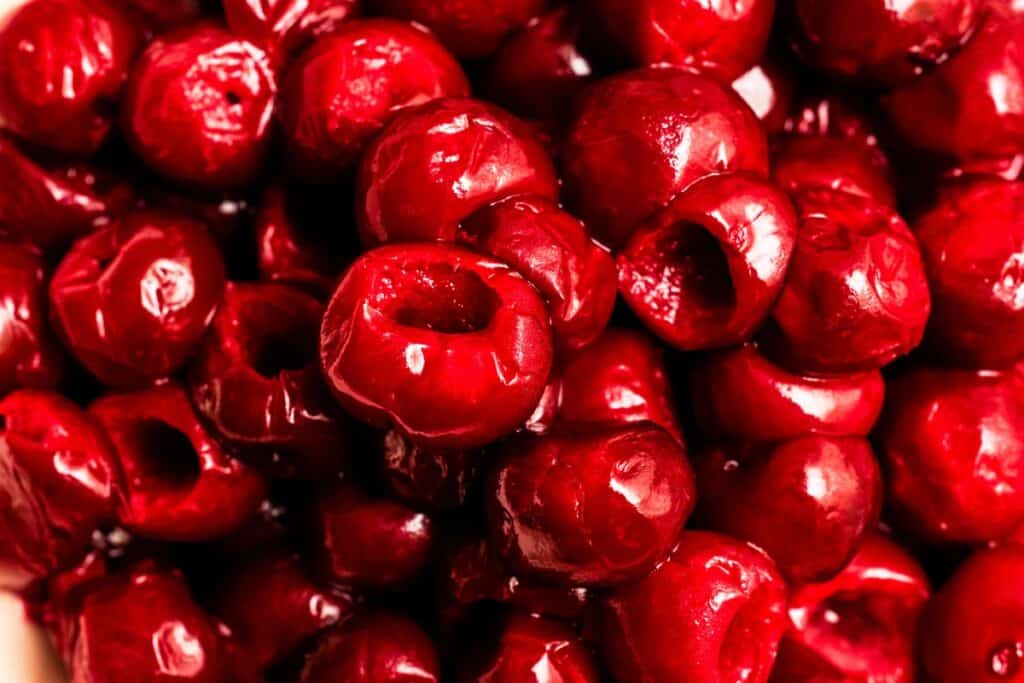 A close-up view of a pile of bright red, pitted cherries. The cherries are glossy and juicy, perfect for a Flaming Cherries Jubilee or any show-stopping flambé dessert. Their hollow centers hint at the first step in a classic Cherries Jubilee recipe.