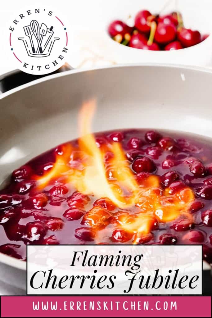 Cherries cook in a pan with orange flames for this striking Flaming Cherries Jubilee. The text "Flaming Cherries Jubilee" and "www.errenskitchen.com" appear, while fresh cherries blur in the background, highlighting this classic flaming dessert.
