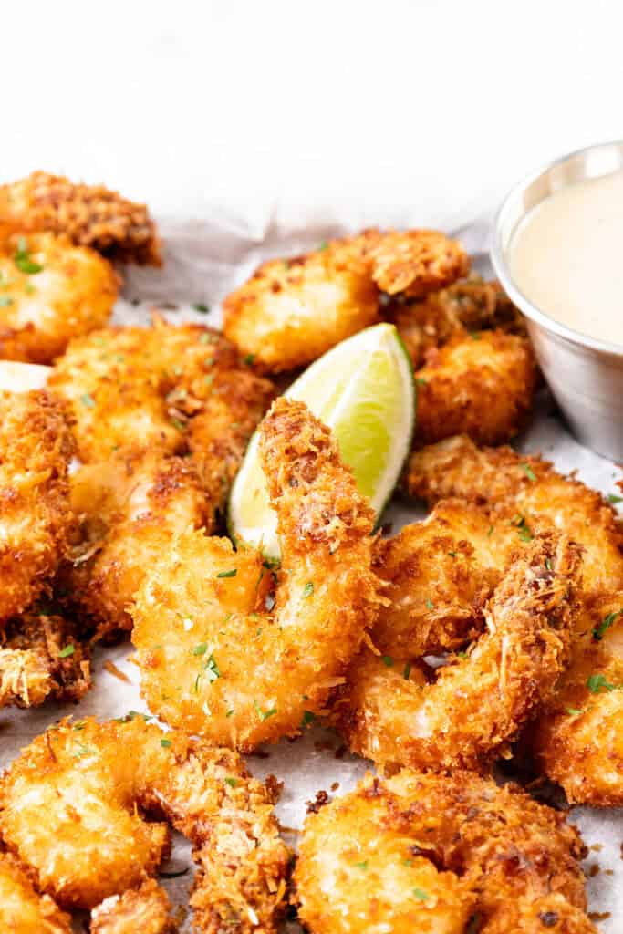 Golden, crispy coconut shrimp garnished with chopped herbs and served with a lime wedge and a small bowl of sweet chili dip—an irresistible coconut shrimp recipe perfect for any seafood lover.