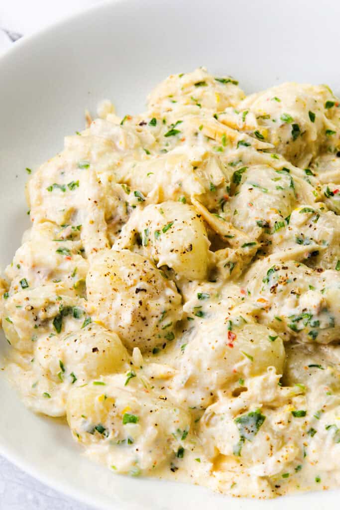 A bowl of creamy crab gnocchi topped with herbs and cracked black pepper, featuring a rich, cheesy sauce mixed with flecks of green herbs.