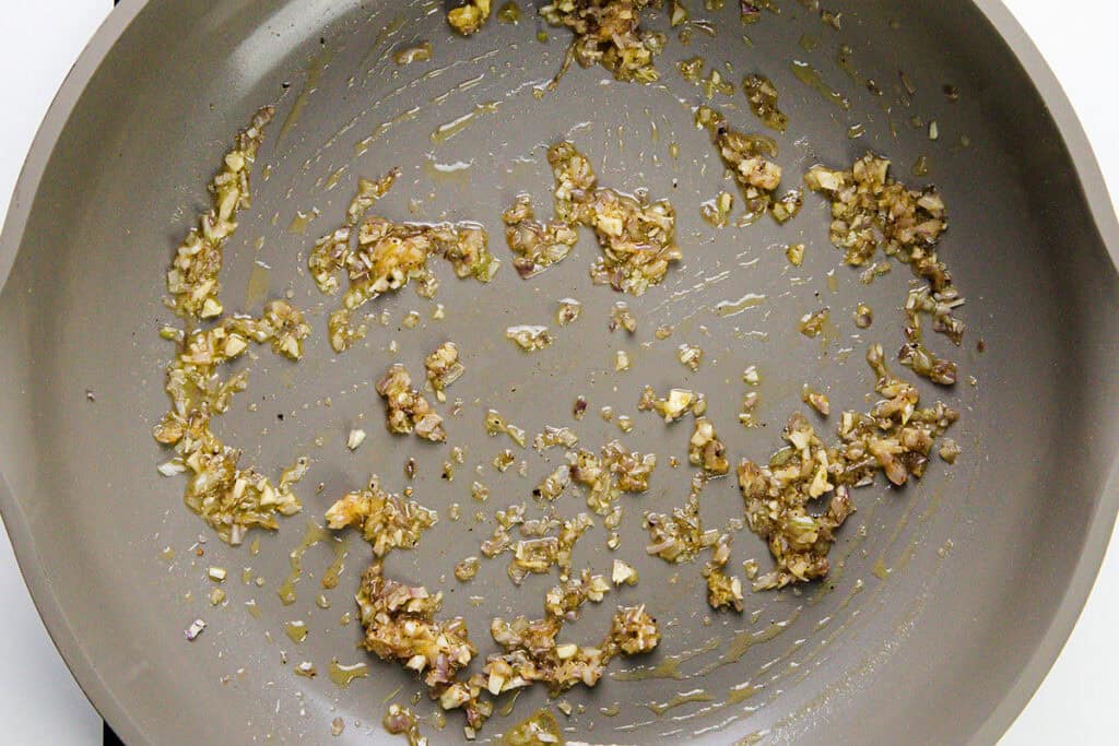 Finely chopped onions and garlic sautéing in oil on a nonstick skillet, beginning to turn golden brown—the perfect base for a creamy gnocchi or delicate crab dish.