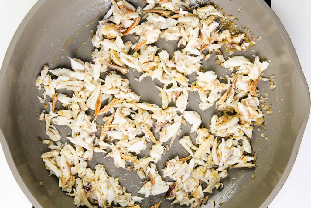 Chunks of crab meat being sautéed in a large gray skillet, lightly browned in parts, with some seasonings visible—perfect for adding to creamy gnocchi or creating your own Creamy Crab Gnocchi dish. The crab pieces are spread out across the pan.