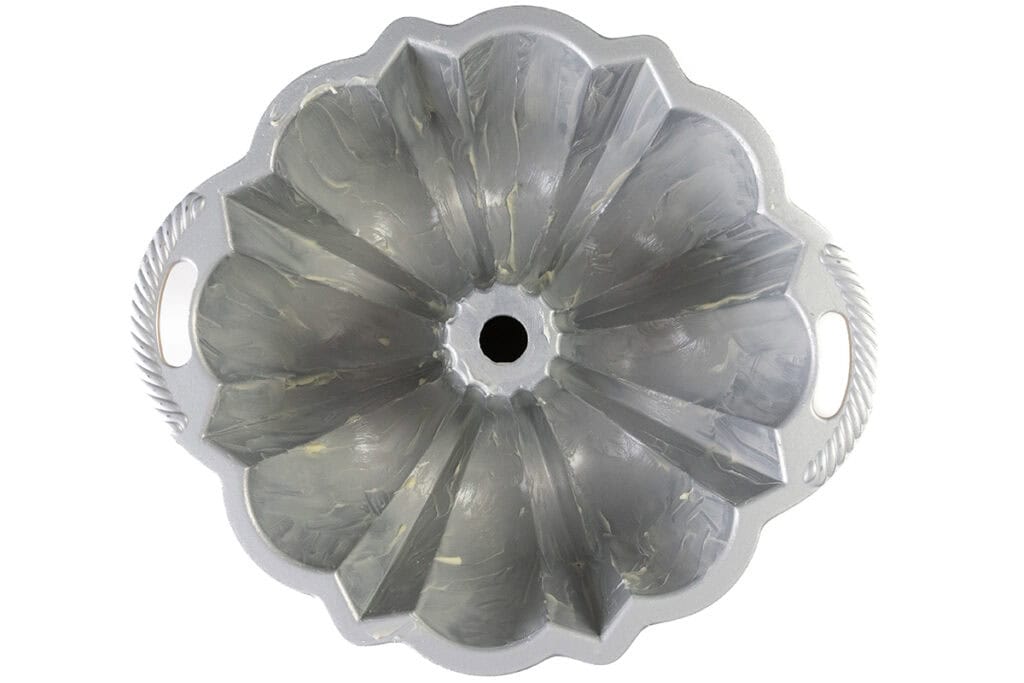 A metal Bundt Cake pan with fluted edges, coated with butter or grease, is shown from above. The pan has handles on both sides and a central tube, ideal for making a filled Bundt Cake or Strawberry Shortcake in a ring-shaped design.