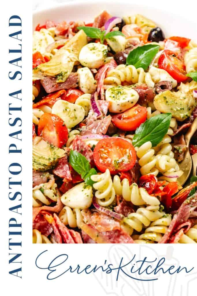 A colorful Italian Antipasto Pasta Salad with rotini, tomatoes, mozzarella balls, olives, salami, artichokes, and basil leaves. "ANTIPASTO PASTA SALAD" and "Erren's Kitchen" text on the side highlight this easy recipe.