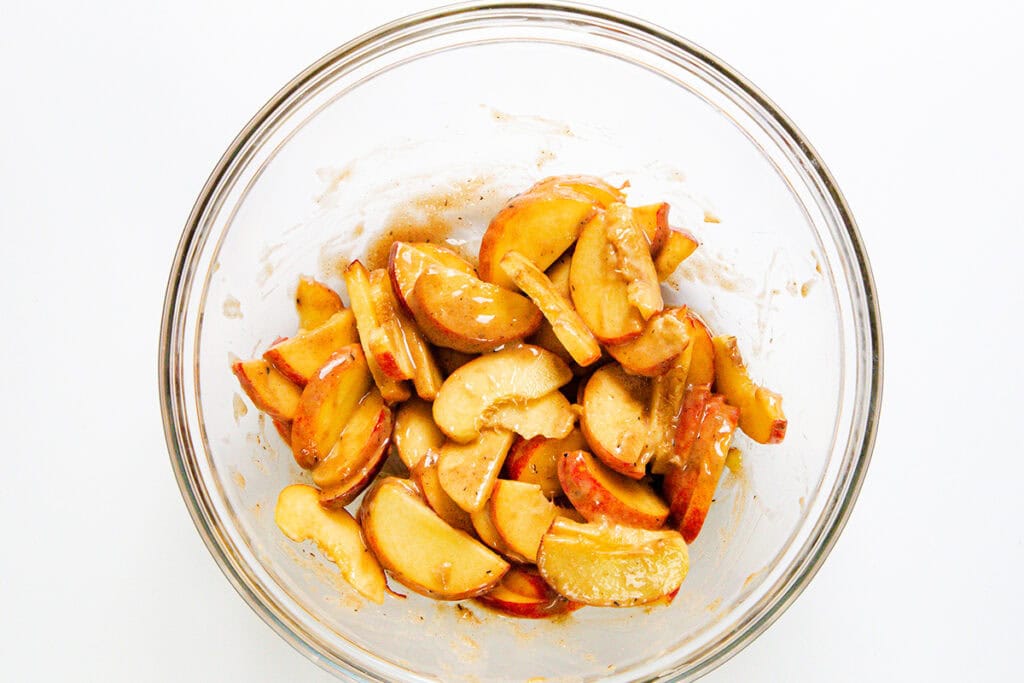 A clear glass bowl filled with sliced apples coated in a cinnamon and sugar mixture, perfect for filling your favorite pie dough, set against a white background.