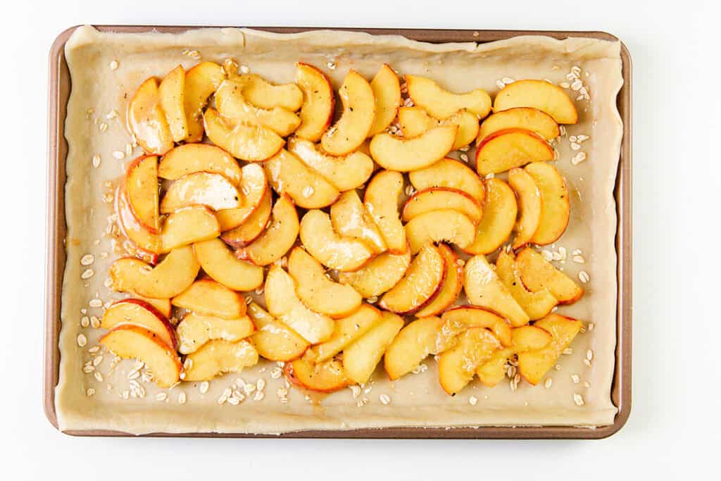 Sliced peaches arranged on a parchment-lined baking sheet, drizzled with a glaze and sprinkled with oats, these tasty treats are perfect for making a rustic peach galette.