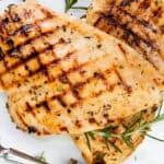 Grilled chicken breast with visible char marks, garnished with fresh rosemary and thyme, served on a white plate with a fork—perfect grilled chicken for any occasion.