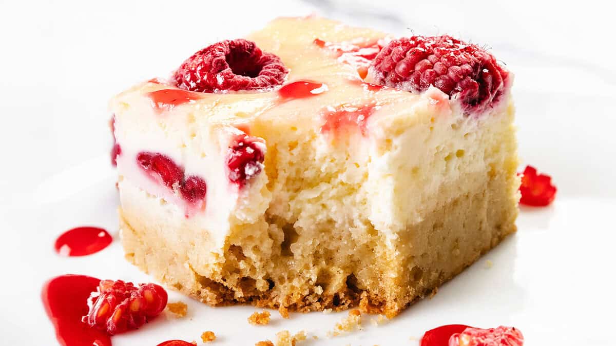 Close-up dari bar cheesecake yang indah dengan kerak yang rapuh, isian krim, raspberry segar, dan gerimis saus raspberry di dalam dan di sekitar kreasi cheesecake yang tak tertahankan ini.