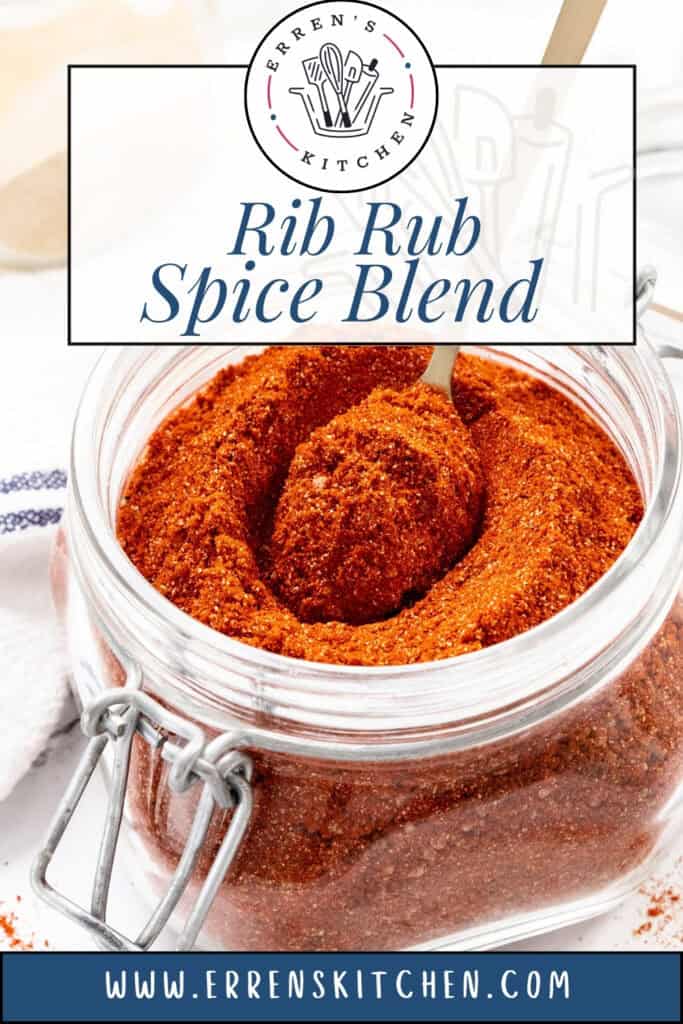A glass jar filled with a reddish-brown Rib Rub Spice Mix, with a spoon scooping some of the blend. The open jar sits on a white surface beside a striped cloth. Text reads “Rib Rub Spice Blend” and “www.errenskitchen.com.”.