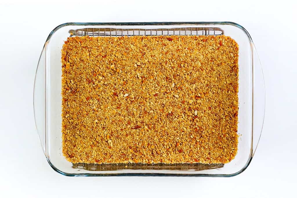 A glass baking dish filled with a golden-brown crumb topping, this strawberry pretzel salad sits on a wire rack against a white background, tempting with its sweet and salty layers.