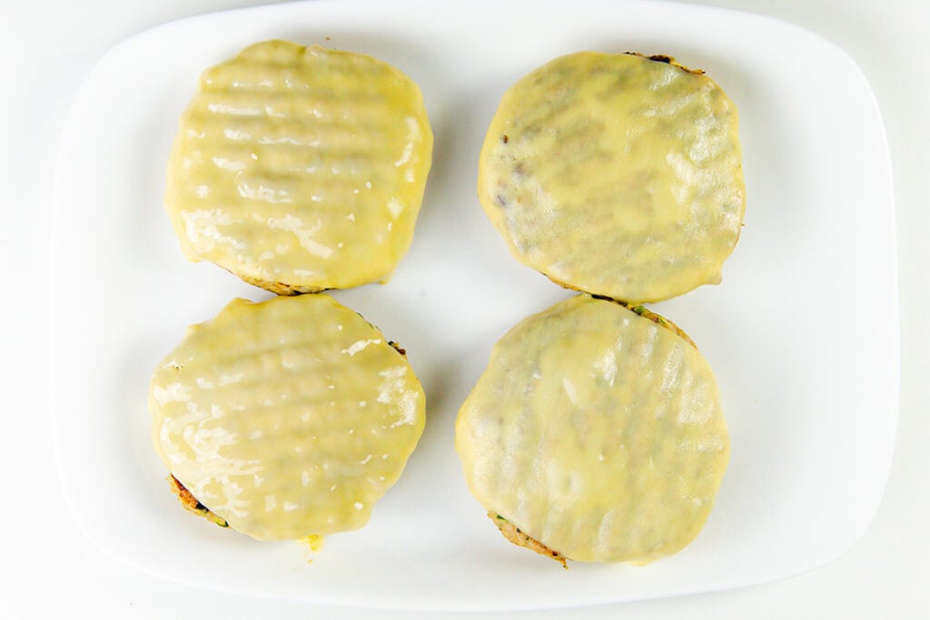 Four moist turkey burgers topped with melted cheese are arranged in a square pattern on a white plate against a white background.