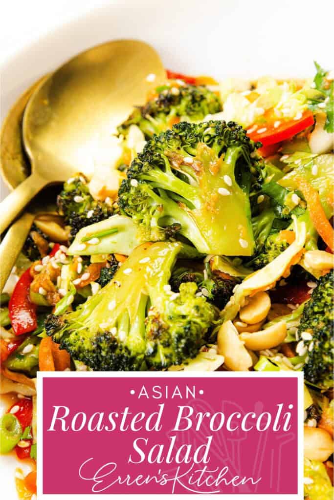 A close-up of roasted broccoli salad with red peppers, shredded carrots, peanuts, sesame seeds, and green onions in a white bowl, served with a gold fork and spoon.