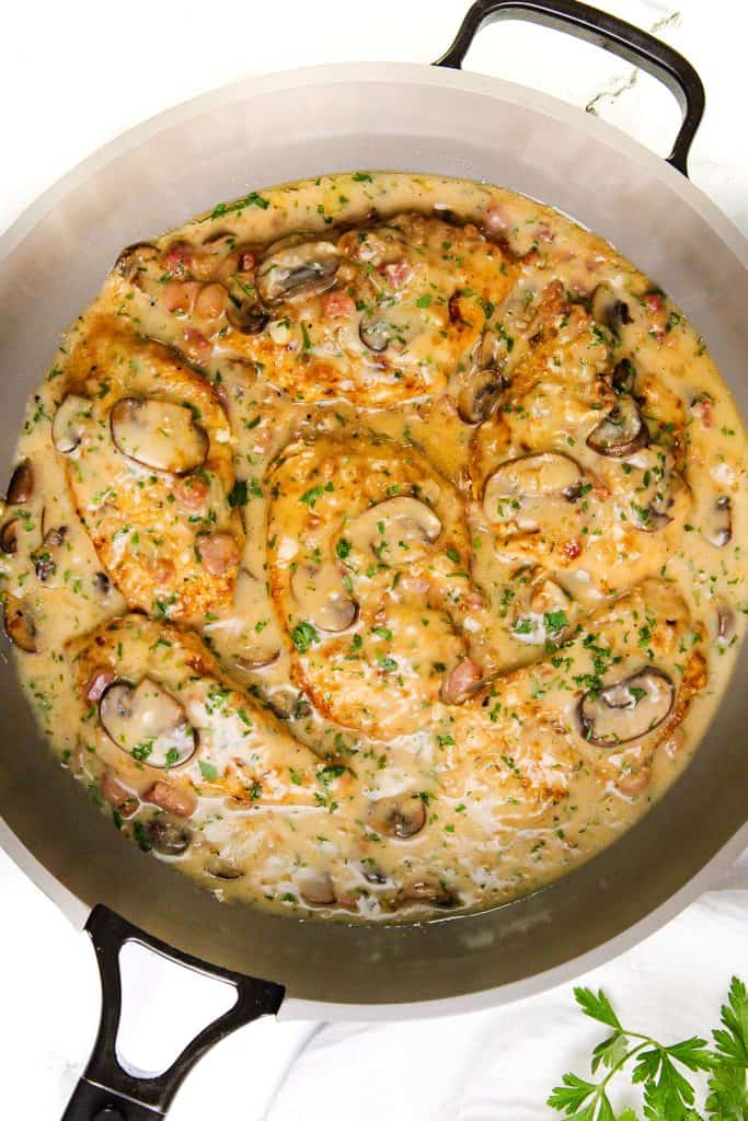 A large skillet filled with pork chops cooked in a creamy mushroom and herb sauce, reminiscent of Creamy Chicken Marsala, and garnished with chopped parsley.