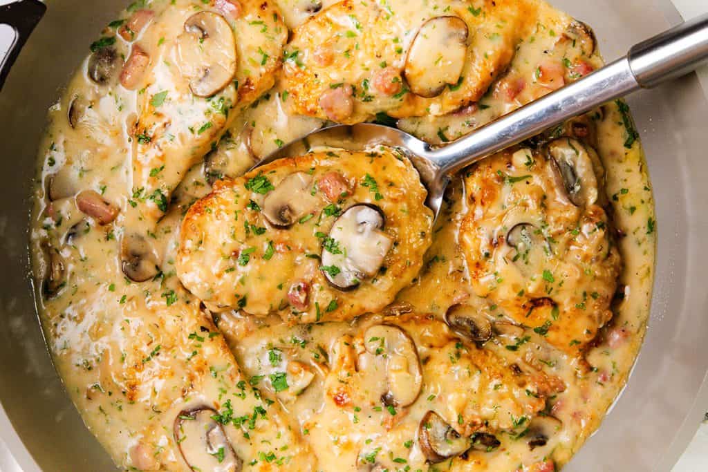 Chicken breasts simmer in a creamy sauce with sliced mushrooms and herbs, topped with chopped parsley—a delicious Creamy Chicken Marsala served in a large pan with a silver serving spoon.