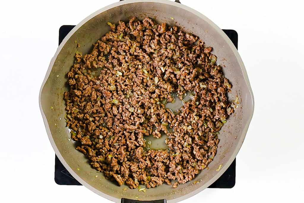A skillet filled with browned ground beef and onion simmers on the stovetop, perfect for starting a creamy ground beef pasta or a hearty one pot pasta dish, with savory juices visible in the pan.