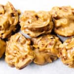 Close-up of several clusters of creamy, golden-brown Southern Pralines candy on a white surface, showcasing their rough texture and visible pecan pieces.