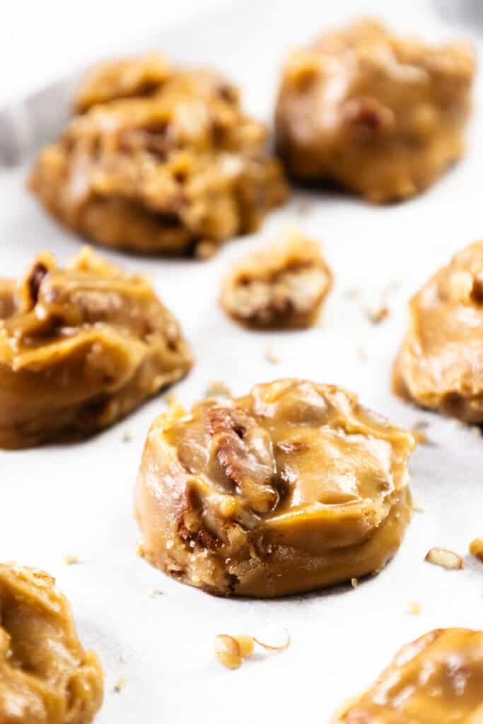 Close-up of homemade Southern Pralines with pecans, featuring several round, golden-brown candies with a glossy, textured surface, arranged on white parchment paper.