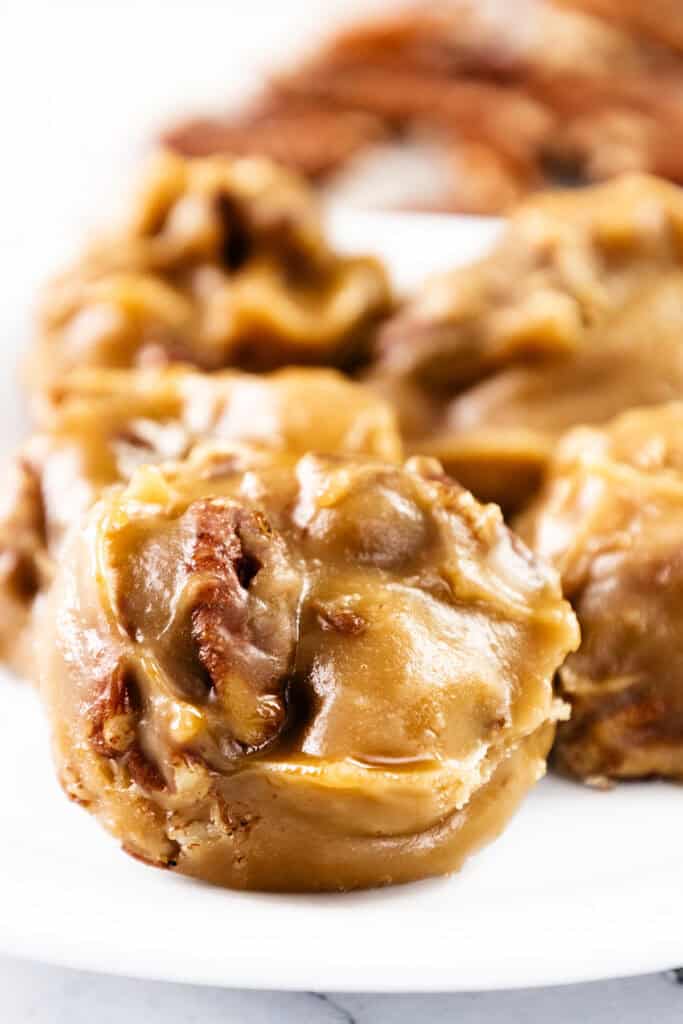 Close-up of creamy, round Southern Pralines with visible pecan pieces, arranged on a white plate. The candies have a glossy, smooth surface and rich caramel color, embodying classic Southern candy tradition.