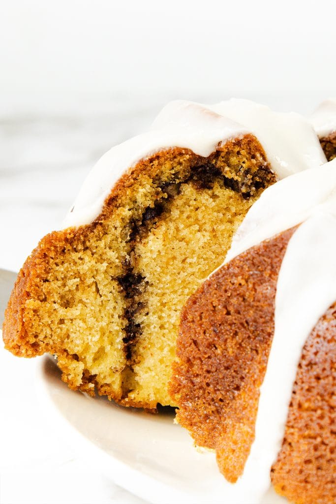 A close-up of a slice of Sock it to me cake, featuring a cinnamon swirl and white icing drizzled on top, displayed on a white plate.