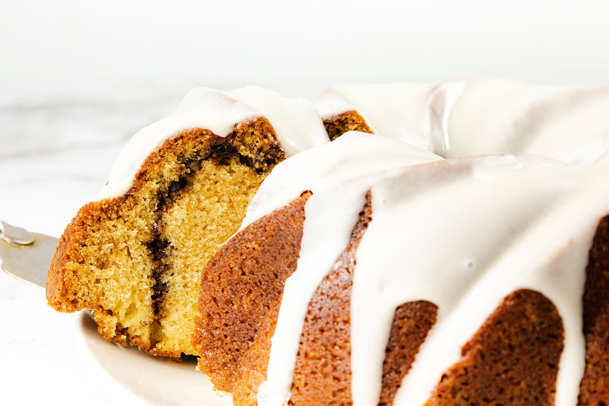 A close-up of a sliced Sock it to me cake with a cinnamon swirl inside and white icing drizzled over the top, displayed on a white plate—an irresistible bundt cake perfect for any cake recipe collection.