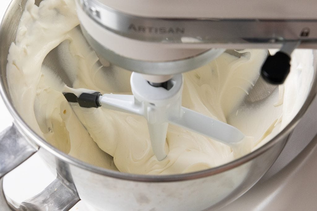 A stand mixer with a paddle attachment mixing smooth, creamy frosting in a stainless steel bowl.