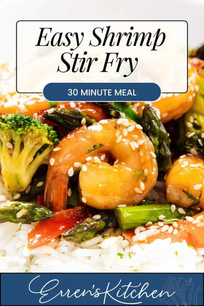 Close-up of shrimp stir fry with broccoli, asparagus, and carrots over white rice, sprinkled with sesame seeds. Text overlay reads "Easy Shrimp Stir Fry, Quick Dinner, 30 Minute Meal, Erren's Kitchen.