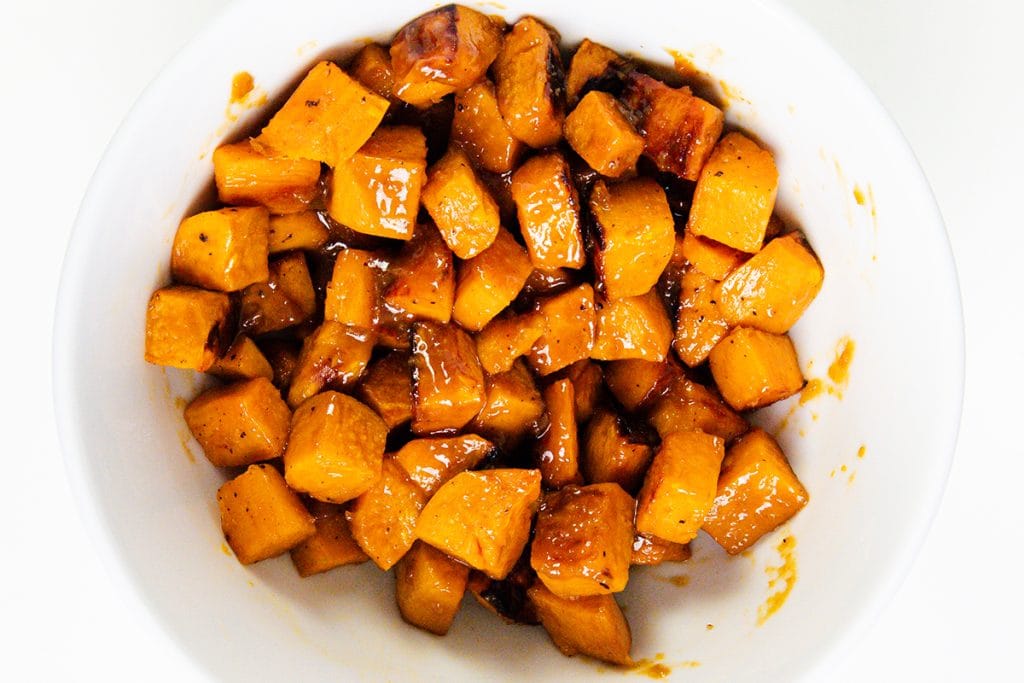 A white bowl filled with miso-glazed sweet potatoes, featuring roasted cubes coated in a shiny, caramelized glaze.