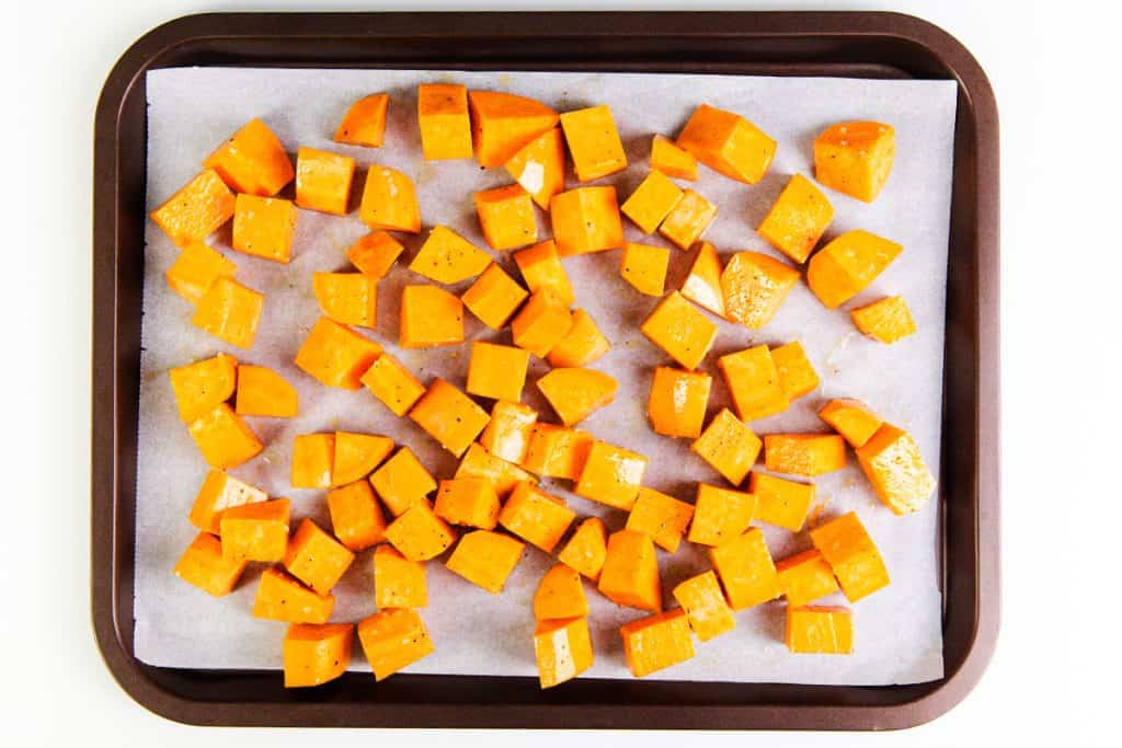A baking tray lined with parchment paper holds evenly spaced, diced sweet potatoes coated in a savory miso glaze, seasoned and ready for roasting.