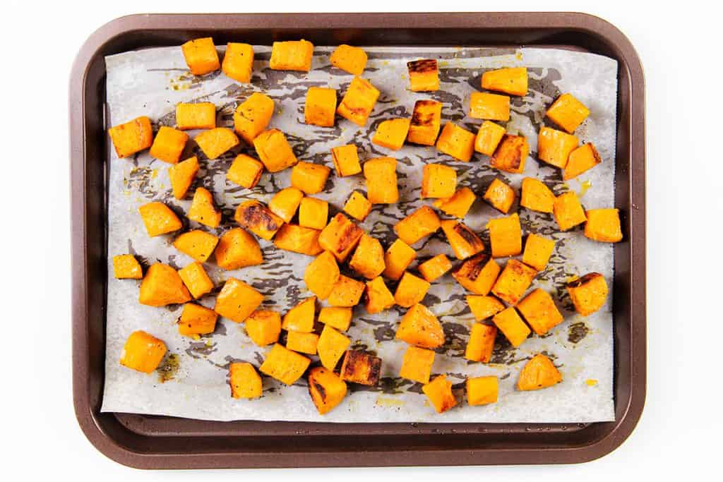 A baking tray lined with parchment paper holds evenly spread, miso-glazed sweet potatoes and roasted butternut squash cubes, all with caramelized, golden-brown edges.