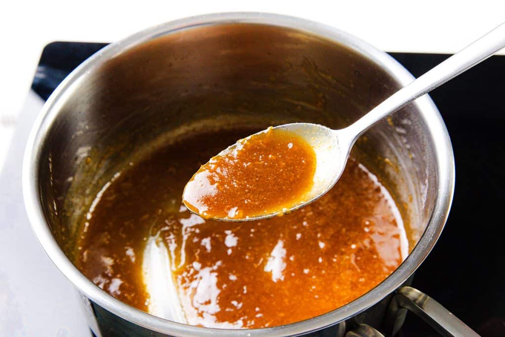 A metal spoon holds up a thick, glossy brown sauce above a saucepan filled with the same Miso-Glazed mixture—perfect for drizzling over Miso-Glazed Sweet Potatoes—simmering invitingly on a stovetop.