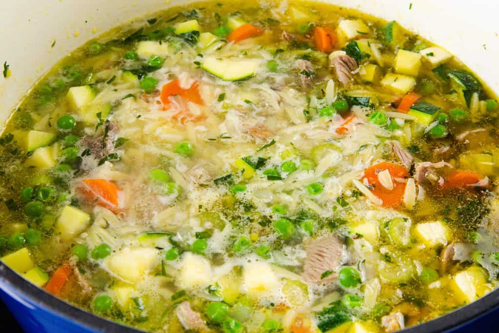 A close-up of a pot filled with orzo soup, showing pieces of carrots, peas, zucchini, and chunks of leftover turkey in a clear broth—an easy and comforting one-pot meal.