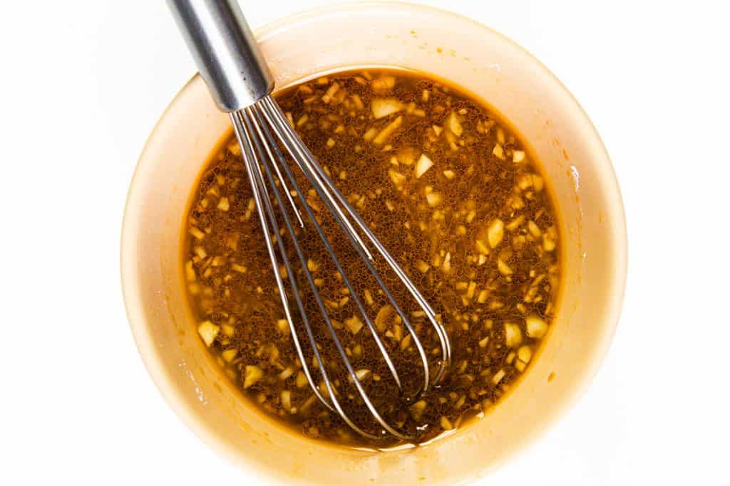 A metal whisk sits in a glass bowl filled with a chunky, golden-brown liquid—perfect as a marinade or sauce for an Easy Shrimp Recipe, with visible pieces of chopped garlic or ginger.
