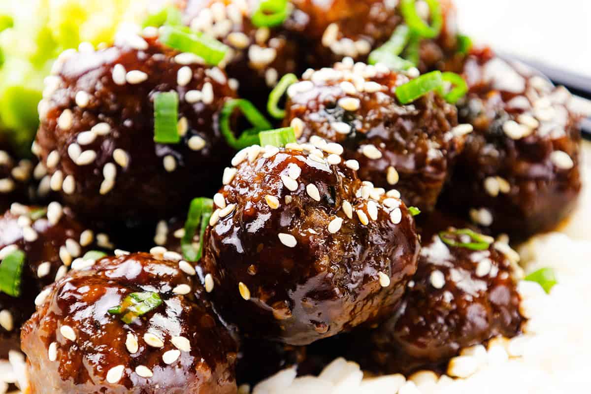 Close-up of Teriyaki Meatballs glazed with teriyaki sauce, topped with sesame seeds and chopped green onions, served on a bed of white rice. Perfect for anyone looking for a flavorful meatball recipe.