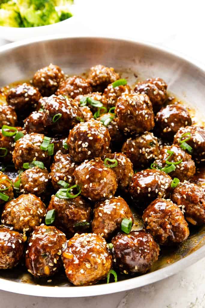 A metal skillet filled with Teriyaki Meatballs, glazed to perfection and garnished with sesame seeds and chopped green onions.