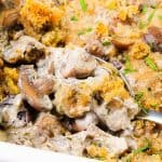A close-up of creamy mushroom casserole topped with golden breadcrumbs and chopped herbs, with a spoon scooping out a portion, highlights the rich texture of this comforting Creamy Mushroom Casserole.