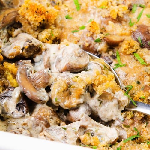 A close-up of creamy mushroom casserole topped with golden breadcrumbs and chopped herbs, with a spoon scooping out a portion, highlights the rich texture of this comforting Creamy Mushroom Casserole.