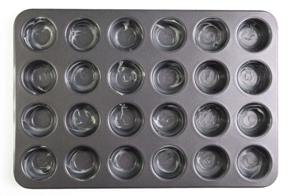 A 24-cup mini muffin pan—perfect for baking Mini Pecan Pie or Pecan Tassies—is lightly greased and viewed from above on a white background.