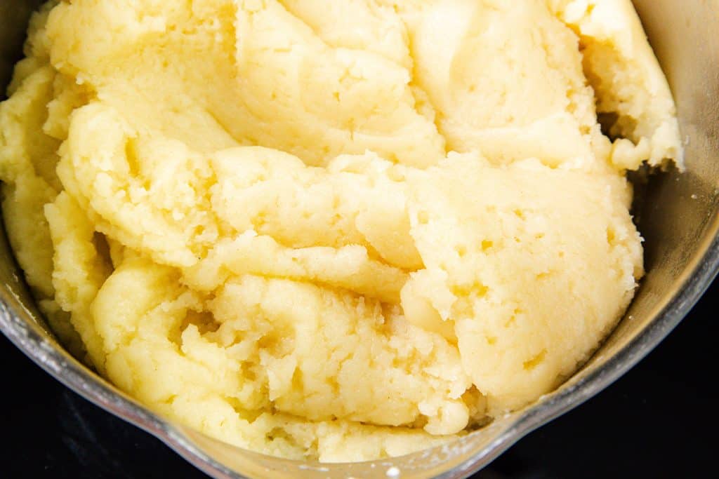 Close-up of a pot filled with pale yellow, smooth Choux Pastry dough—perfect for cream puffs—showing its soft and slightly smooth texture.