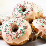 A plate of baked donuts topped with white icing and festive red, green, and white sprinkles, arranged in a pile on a white plate—perfect Christmas donuts for your holiday celebrations.