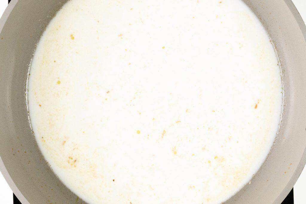 A close-up view of a saucepan filled with a white, milky liquid being heated, possibly for a One Pot recipe like Lemony Shrimp Orzo, with small yellowish specks throughout.