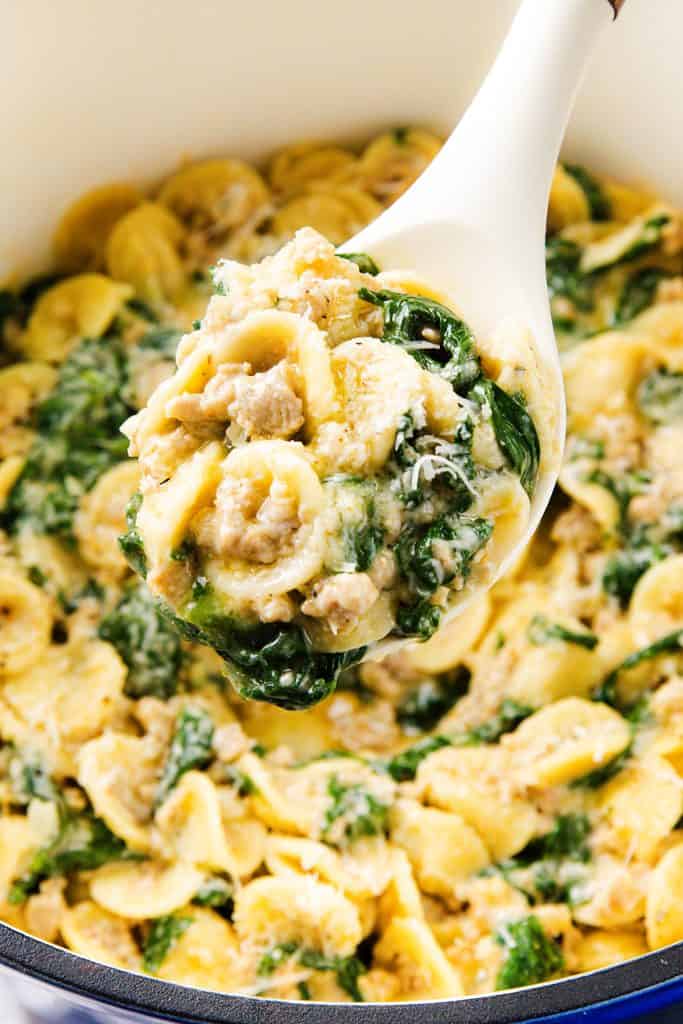 A close-up of a spoonful of creamy sausage orecchiette with spinach being lifted from a pot, showcasing the deliciously rich one-pot pasta dish.