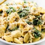 A white bowl filled with creamy sausage orecchiette pasta, spinach, and ground meat, topped with grated parmesan cheese and red pepper flakes. A gold fork rests on the side of this inviting one-pot recipe.