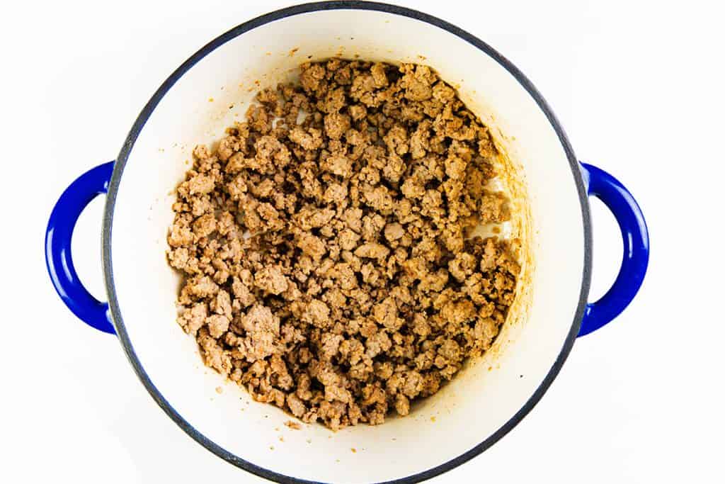 A blue-handled pot filled with cooked and crumbled seasoned sausage, perfect for starting a flavorful One-Pot Pasta or Creamy Sausage Orecchiette, shown from above on a white background.