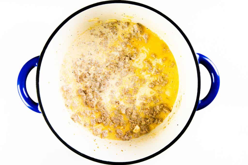 Ground sausage cooking in a white pot with a blue rim, mixed with a creamy yellow sauce—a delicious base for creamy sausage pasta.