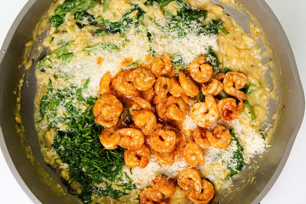 A creamy one pot risotto topped with lemony shrimp, grated cheese, spinach, and fresh herbs in a pan. The dish looks freshly cooked and colorful.