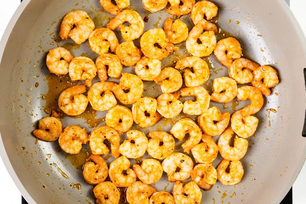 Lemony Shrimp coated in a reddish seasoning are spread out in a large skillet, glistening with oil and spices—perfect for an easy one pot meal.