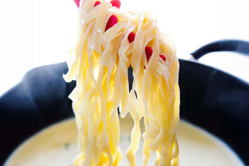 Tampilan jarak dekat dari masakan yang dicelupkan ke dalam panci berisi saus krim.